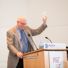 Art Gelb at a lectern holding up a small glass trophy in the shape of an X