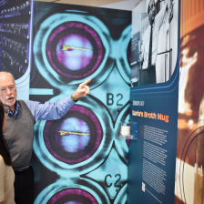 Two people discuss an exhibit wall displaying a ceramic mug 