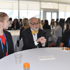 Matthew Frosch talks with two students seated at a round table bearing food and beverages.