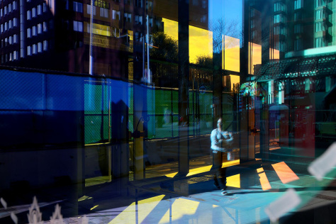 A woman’s reflection is seen through a colored sticker adhered to a window in Kendall Square.