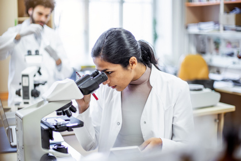 a woman in a lab coat peers into a microscope